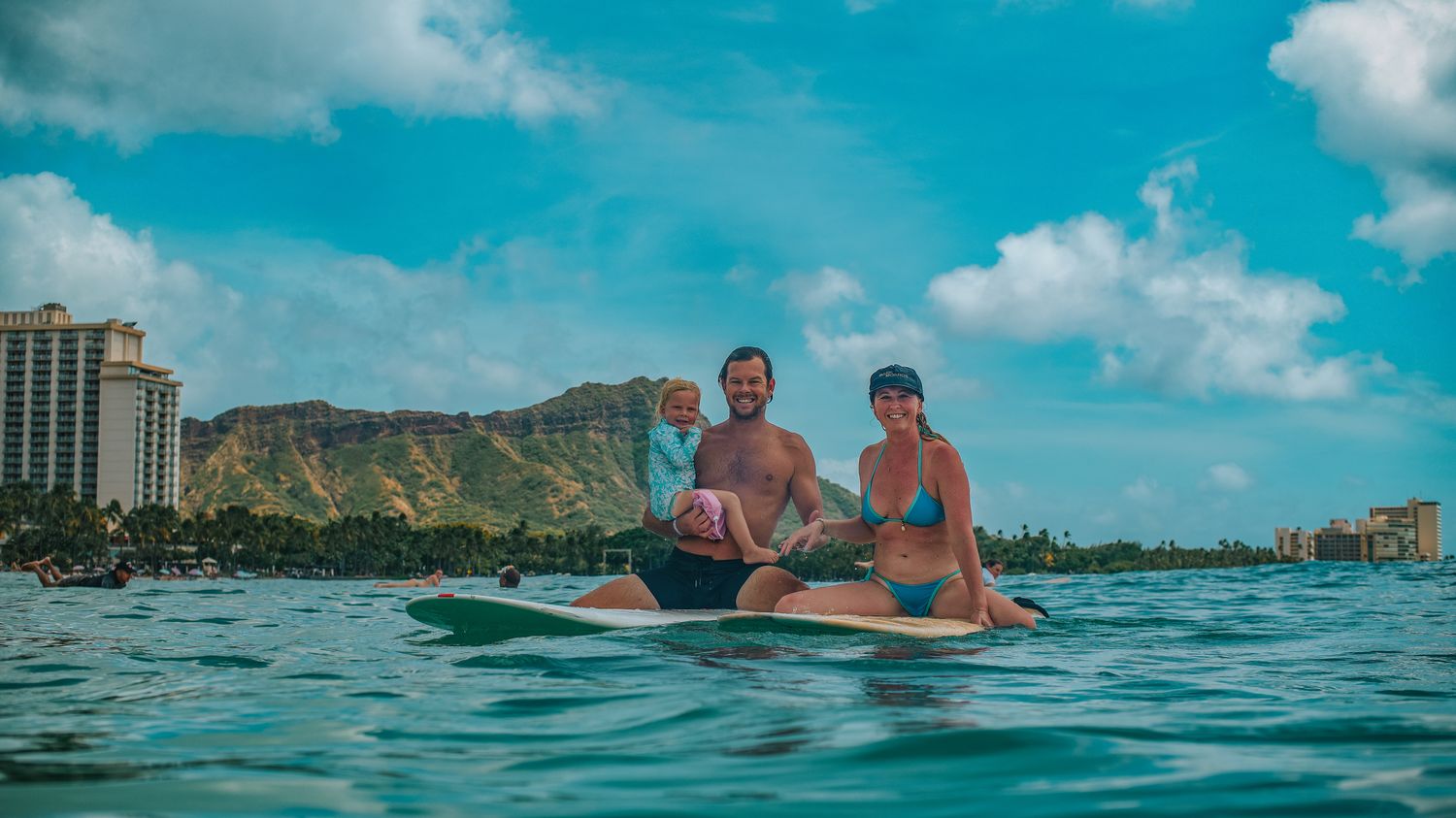 Family with a young daughter sitting on surfboards off Waikiki, Diamond Head behind