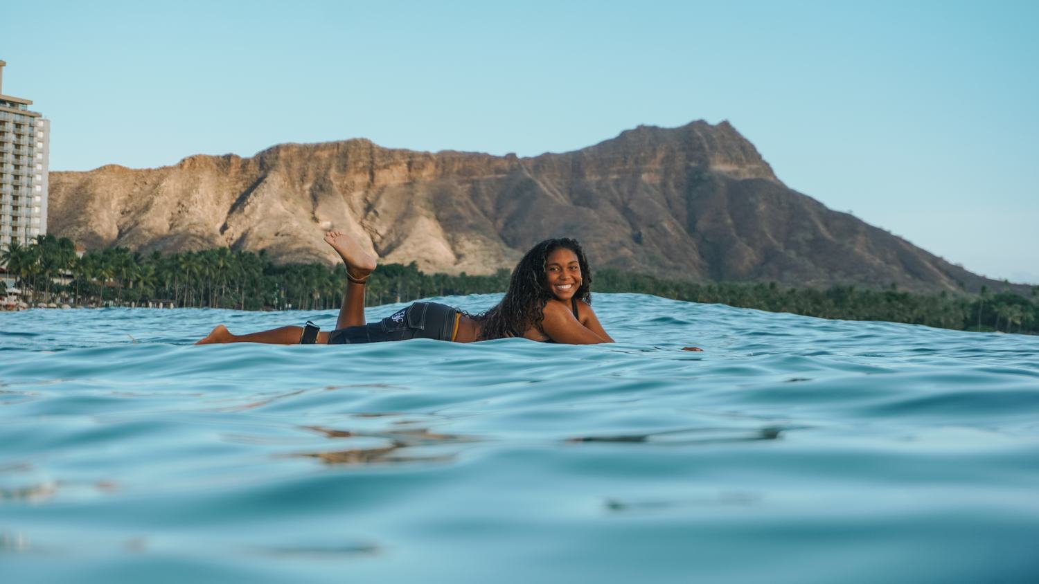 Woman lying on surfboard with foot raised, laughing