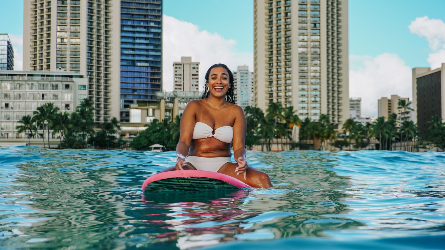 Woman laughing on surfboard with city skyline