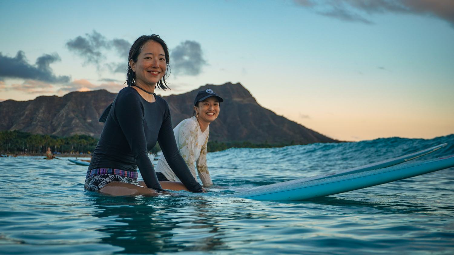Two women smiling on a paddleboard with Diamond Head behind