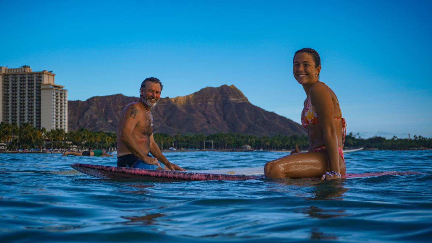 Man and woman sitting on a paddleboard with Diamond Head behind