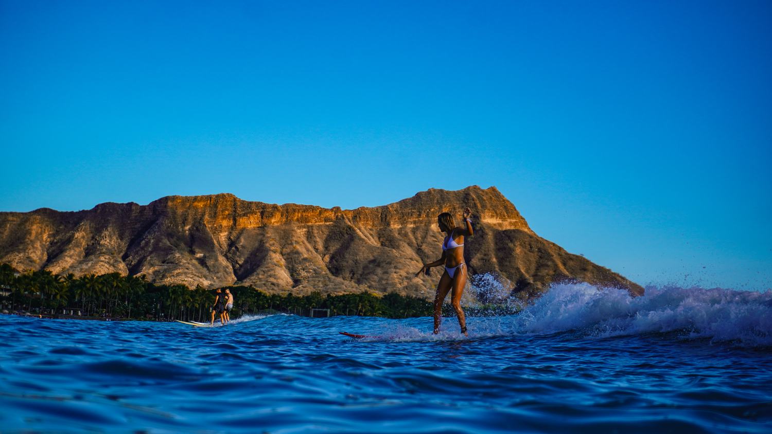 Silhouette of a woman surfing at dusk, arm raised