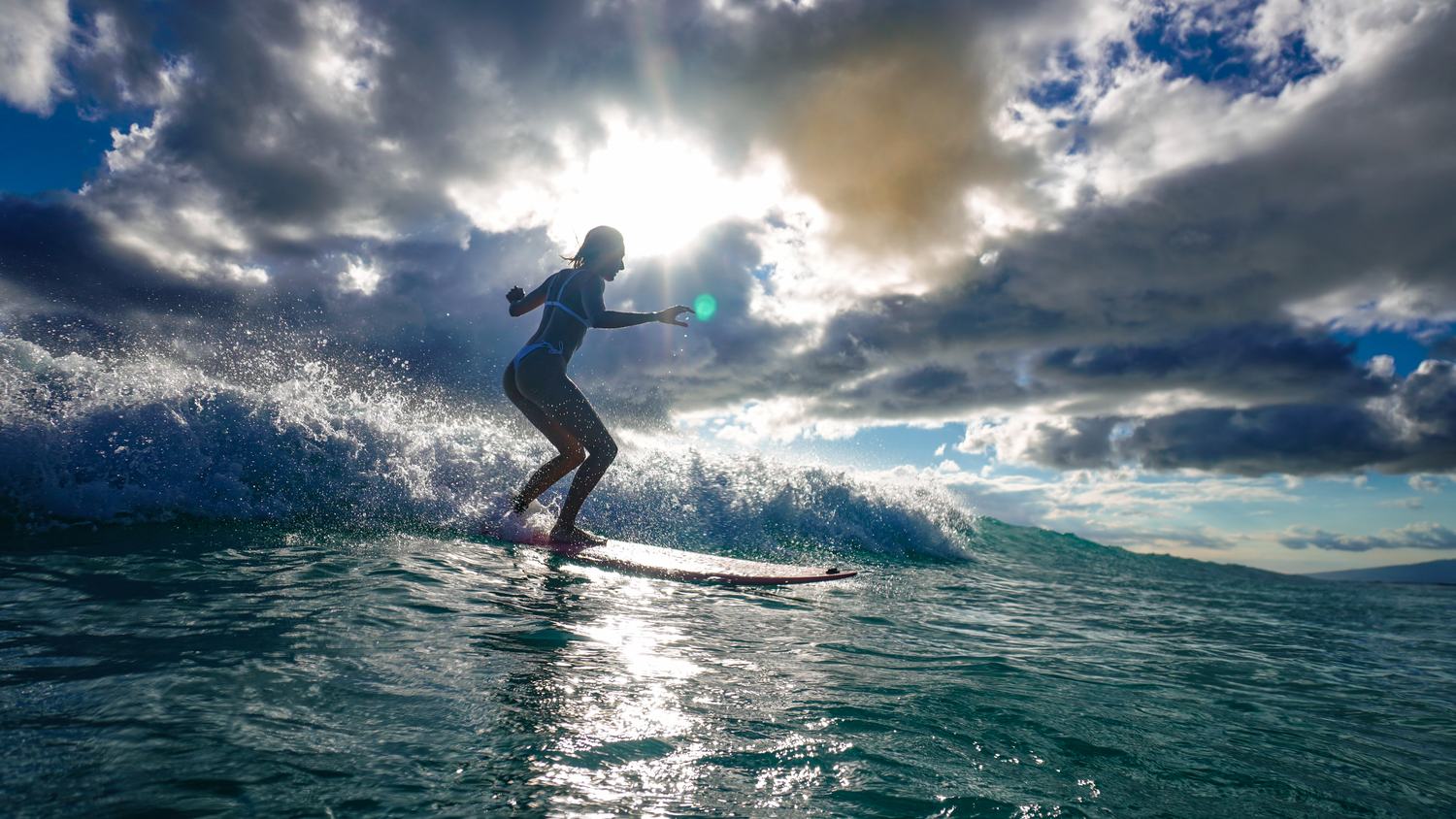 Woman surfing with dramatic sunburst through clouds